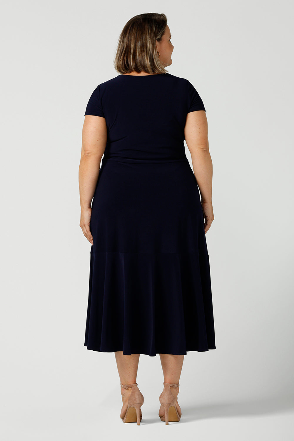 If you're looking for dresses made in Australia, look to this elegant navy dress shown on a curvy, size 18 woman as a plus size dress. Shown from the back, this high neck, short sleeve dress with flared skirt and ruffle hemline is a good workwear dress as well as a classic cocktail dress. With a midi-length skirt, shop this dress in plus sizes as well as petite thanks to made-in-Australia, ethical  ladies clothing brand, Leina & Fleur