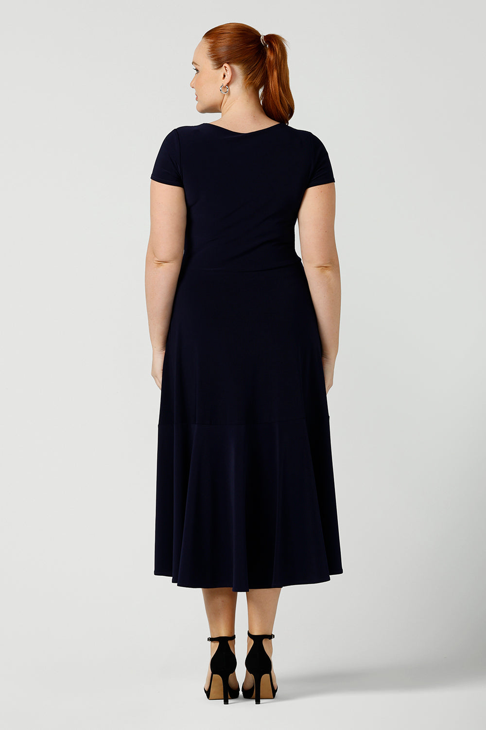 Back view of an Australian-made navy dress in size 12, shown for curvy. This high neck, short sleeve dress with flared skirt and ruffle hemline is a good workwear dress as well as a classic cocktail dress. With a middi-length skirt, shop this dress in plus sizes as well as petite thanks to made-in-Australia women's clothing brand, Lena & Fleur.