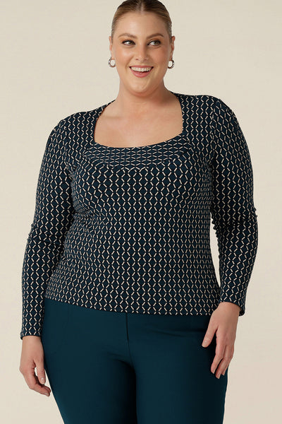 A plus size, size 18 woman wears a long sleeve tops with squared scoop neckline. In geometric print jersey, this comfortable top is good for work wear capsule wardrobes. Made in Australia, shop tops in sizes 8 to 24.