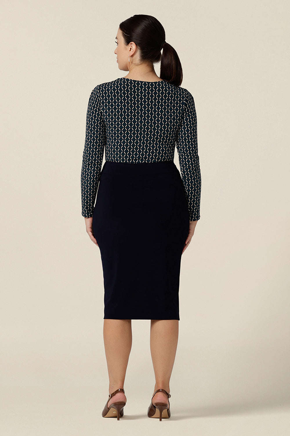 Back view of a good work top for corporate capsule wardrobes, this long sleeve top has a squared scoop neckline and blue and white geometric print. Worn with a navy blue pencil skirt, both are made in Australia. This office wear top is ready to shop in sizes 8 to 24.