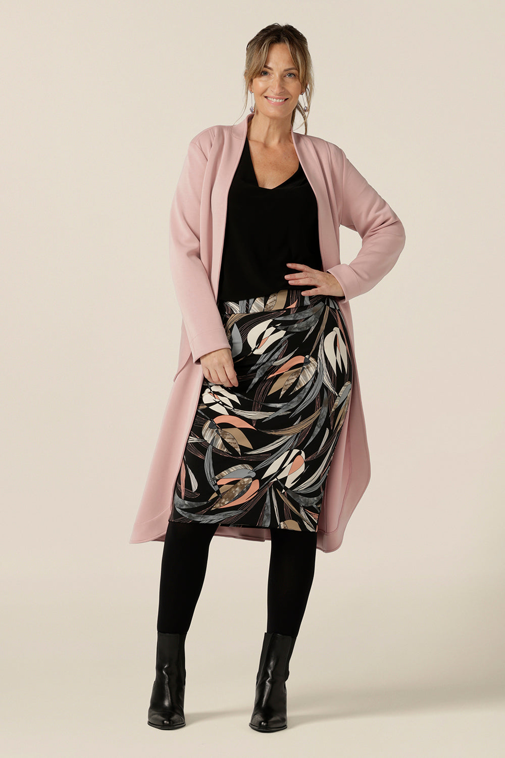 A woman wears a knee-length, tube skirt in floral print stretch jersey, size 10 with a long sleeve, black V-neck top and pink trenchcoat.  A good skirt for work and casual wear , this tube tube skirt is made in Australia by Australian and New Zealand women's clothing brand, L&F.