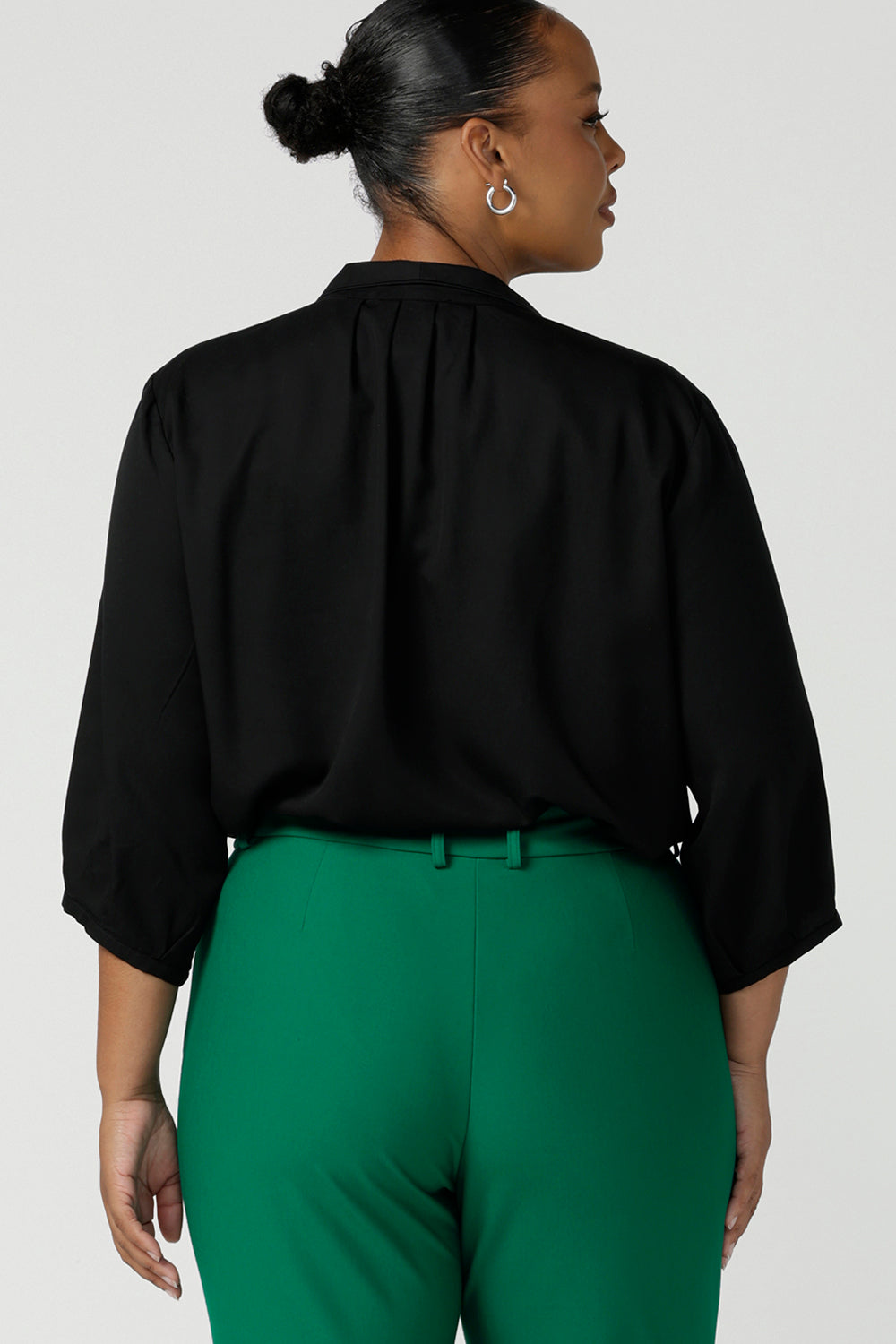 Back view of a size 18 curvy woman wearing a pull-on black shirt with 3/4 sleeves in eco-friendly Tencel. The shirt is worn with emerald green pants for a classic work wear look. This black shirt is made in Australia for petite to plus size women.