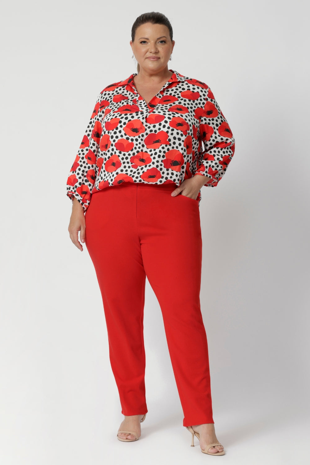 The semi-fitted silhouette ensures a flattering shape without being too tight, offering ease of movement for all-day wear. Below the back neckline, tuck details add an element of interest and elevated tailoring. Size 18 woman wear red printed blouse with tangerine coloured pants for a statement workwear outfit. 