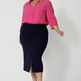 Full body front view of 40 year old plus sized woman wearing a midi length work skirt. This workwear skirt is navy in colour and made of good quality scube crepe fabric. This skirt has an above the knee slit for comfort and mobility. Perfect skirt for an office or corporate setting. 3/4 length skirt is Australia made by New Zealand and Australian women. Leina & Fleur is a clothing company for woman that stock sizes from 8 to 24. Shop this work skirt in plus sizes and petite sizes. 