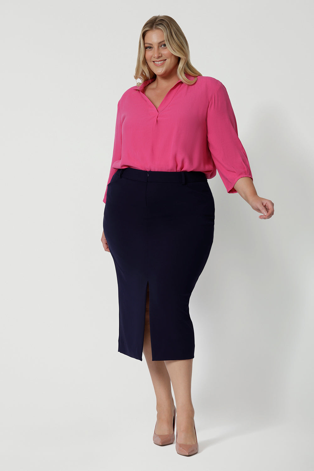 Showing a great work shirt for plus size women, a curvy woman wears a pink tencel fabric shirt in size 18. Workwear shirt displays 3/4 length sleeves tucked into a navy skirt. This collared shirt is made from tencel fabric made in Australia by Australian and New Zealand women. Woman’s clothing brand Leina & Fleur stock sizes from 8 to 24 including plus sizes and petite sizes.