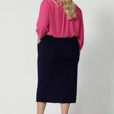 Full body back view of plus sized model wearing 3/4 length skirt. Work skirt is made of easy to care fabric in scube crepe fabric. Workwear skirt has a deep navy colour. This comfortable work wear skirt provides full body stretch great for any office or corporate setting. Australia made clothing. Made by Australian and New Zealand women. Leina and Fleur is a woman’s fashion label that stocks sizes from 8 to 24. Shop this appropriate work skirt in plus size and petite sizes. 