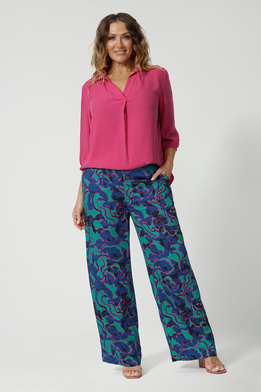 Full body image of an over 40 year old woman wearing a pink tencel fabric shirt with 3/4 length sleeves tucked into a patterned pant. This collared shirt is made from tencel fabric made in Australia by Australian and New Zealand women. Woman’s clothing brand Leina & Fleur proudly stock sizes from 8 to 24 including plus sizes and petite sizes for all. 