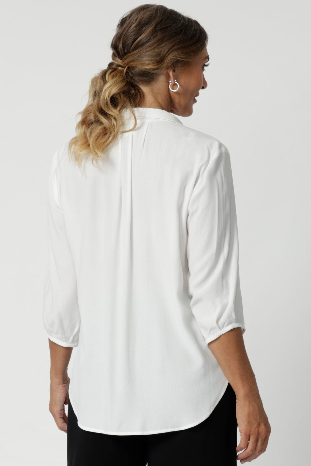 Back view image of size 12 woman wearing the Arley Shirt in in Vanilla. A soft tailored shirt with 3/4 sleeves, collar neckline and shirttail hem. Pull on shirt is made in Australia of sustainable tencel fabric. Soft and easy care workwear for women for petite to plus size 8-24. Styled back with a Bradley culotte in navy. 