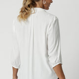 Back view image of size 12 woman wearing the Arley Shirt in in Vanilla. A soft tailored shirt with 3/4 sleeves, collar neckline and shirttail hem. Pull on shirt is made in Australia of sustainable tencel fabric. Soft and easy care workwear for women for petite to plus size 8-24. Styled back with a Bradley culotte in navy. 