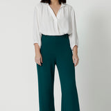 Showing good workwear pants for petite women,  Green scuba crepe wide leg pants are worn with a white work shirt. These wide leg work trousers are made in Australia by Australia and New Zealand women's clothes brand, Leina & Fleur. Available to shop in sizes 8 to 24, this is workwear for plus size to petite height women. 