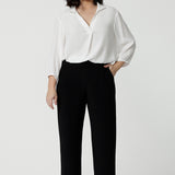 A petite height woman wears black work pants in petite length with a white tencel shirt. Great pants for short women, these Australian-made pull-on trousers are available in sizes 8 to 24, petite to plus sizes.