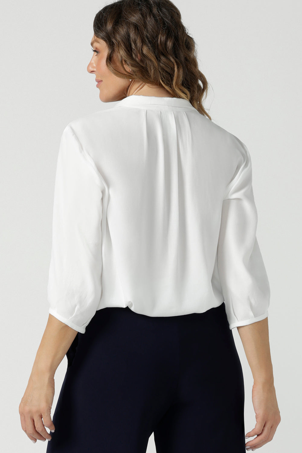 A size 10 woman wears the Arley Shirt in in Vanilla Tencel. A soft tailored shirt with 3/4 sleeves and collar neckline. Made in sustainable tencel fabric. Soft and easy care workwear for women for petite to plus size 8-24. Made in Australia. Styled back with a Bradley culotte in navy. 