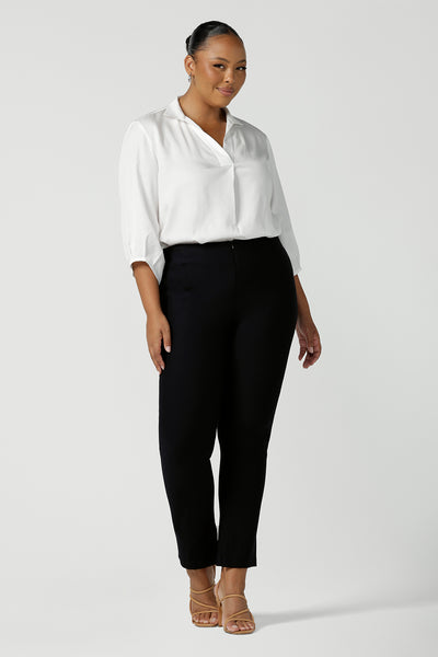Size 18, fuller figure woman wears mid-rise, slim leg navy pants by Australian and New Zealand women's clothing label, L&F. These skinny workwear trousers have a concealed zip fastening and side pockets. Worn with a 3/4 sleeve white women's shirt. Shop these navy workwear pants in an inclusive size range of 8 to 24.