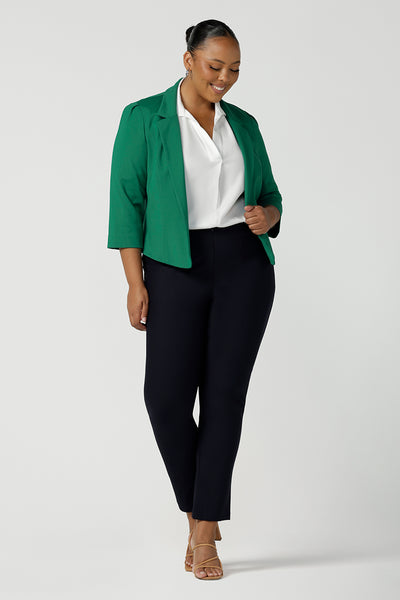 A plus size 18 woman wears a tailored jacket with open front and collar and notch lapels is made in Emerald green ponte fabric. Styled with fitted navy pants, and a white shirt for a stylish workwear look. Shop exclusive luxury, this work jacket is available at Australian and New Zealand women's clothing label, L&F.