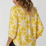 Back view of image woman's work shirt in soft light yellow shade. Made of high quality tencel viscose fabric, it provides the woman on the go a lightweight and comfortable work top. This shirt feature a fresh and uplifting yellow tone, complemented by a subtle white design. Woman's fashion brand stocks this top in sizes 8-24.