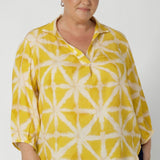 Plus sized woman wears bright yellow shirt that features a simple design that adds a touch of modern flair. Crafted from eco-friendly tencel fabric, it offers a soft and breathable feel, perfect for both comfort and sustainability. Available in size 8-24.