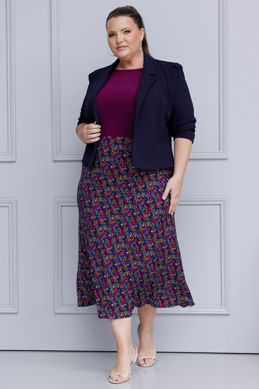 Size 18 woman wears workwear midi skirt paired with magenta top and navy jacket for an elevated workwear look. Crafted on floral dry touch fabric, this skirt features a bias-cut design that drapes beautifully, creating a flattering, easy fluid silhouette. Available in sizes 8-24.