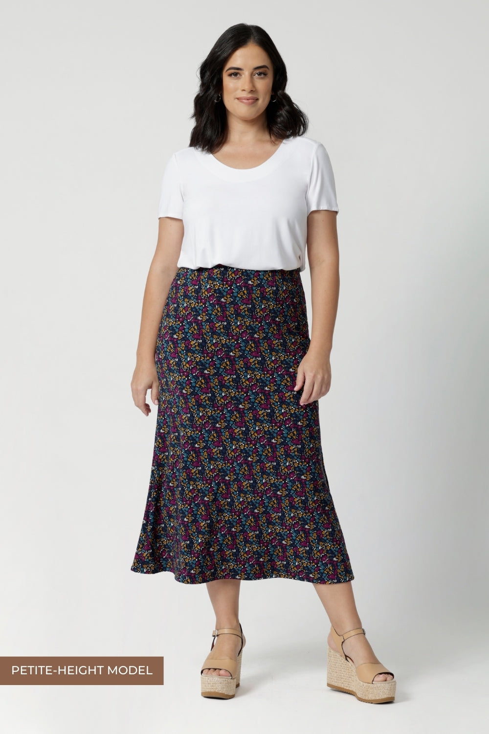 Petite height model wears midi skirt that offers a lightweight feel that's perfect for all-day comfort. Size 10 woman wears travel ready skirt with white t-shirt and platform shoes.