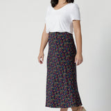 Side view image of petite height woman wearing floral midid skirt paired with white top and platform heels creating an easy care, easy wear summer outfit. Woman's clothing brand Leina & Fleur stock these midi skirts in sizes 8-24 with the options of 4 different colours & shades.