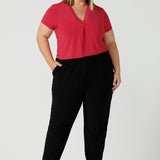 Curvy size 18 woman wears jersey work pants in black. Styled back with a fuchsia pink v-neck top. Comfortable corporate pants for women. Designed and made in Australia for women sizes 8 - 24. 
