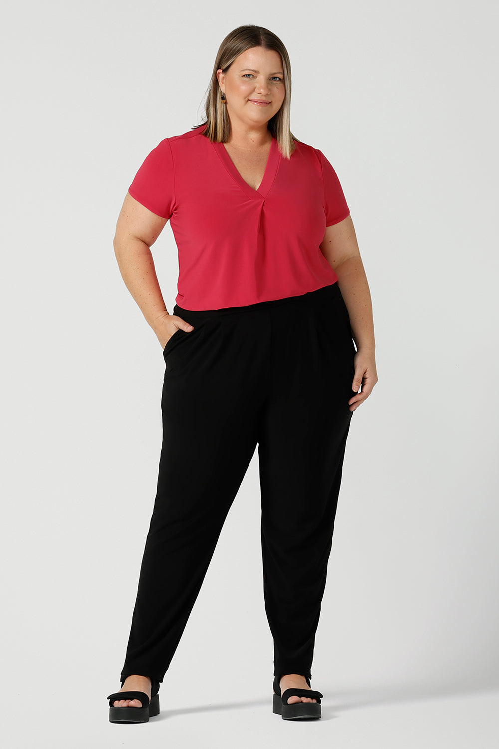 Curvy size 18 woman wears jersey work pants in black. Styled back with a fuchsia pink v-neck top. Comfortable corporate pants for women. Designed and made in Australia for women sizes 8 - 24. 