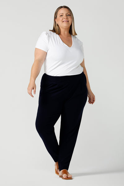 A curvy size 18 woman wears jersey work pants in navy. Styled back with a white bamboo v-neck top. Comfortable corporate pants for women. Designed and made in Australia for Australian womenswear label Leina & Fleur. Inclusive size range 8 - 24.