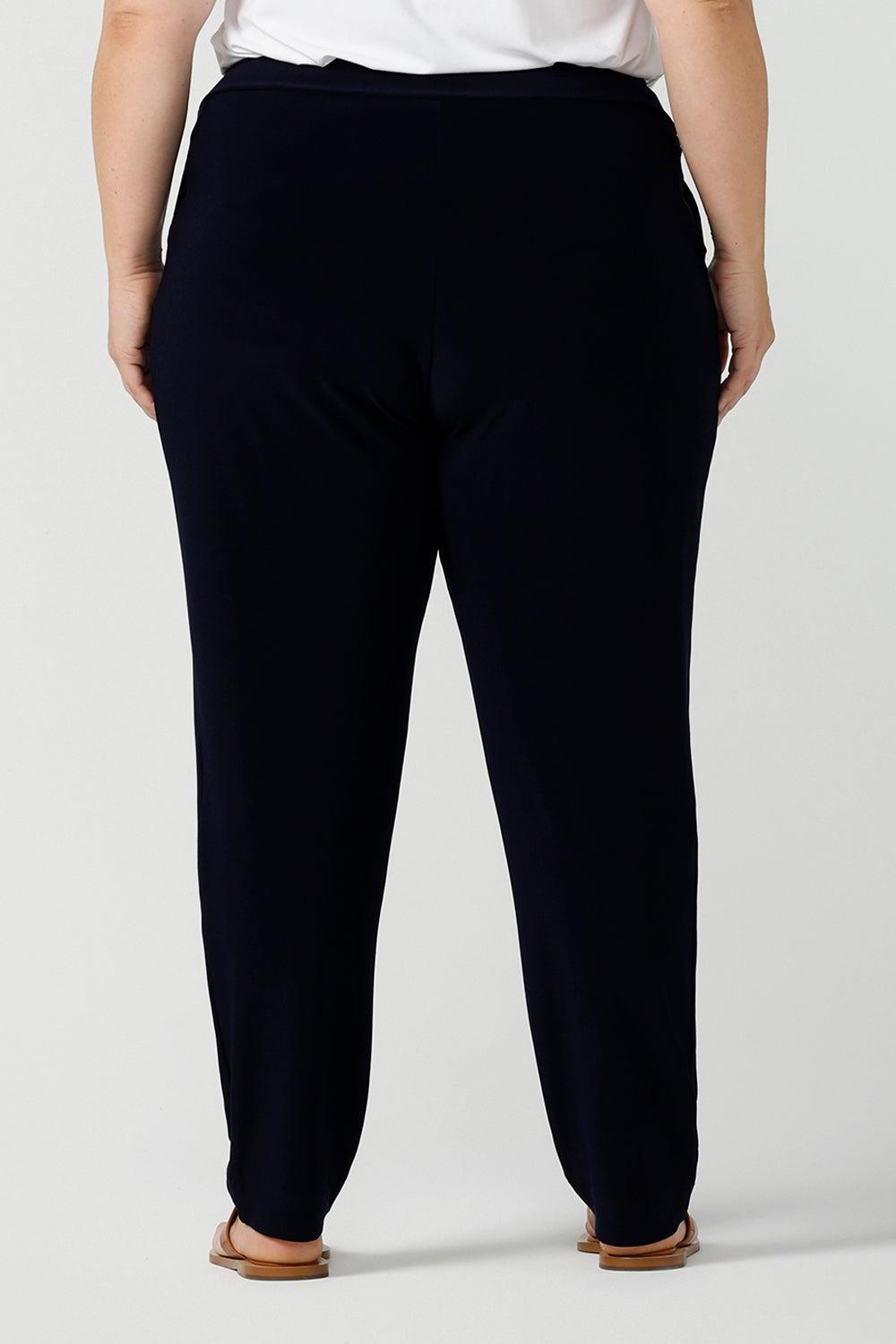 Close up back view of curvy size 18 woman wears jersey work pants in navy. Styled back with a white bamboo v-neck top. Comfortable corporate pants for women. Designed and made in Australia for Australian womenswear label Leina & Fleur. Inclusive size range 8 - 24.