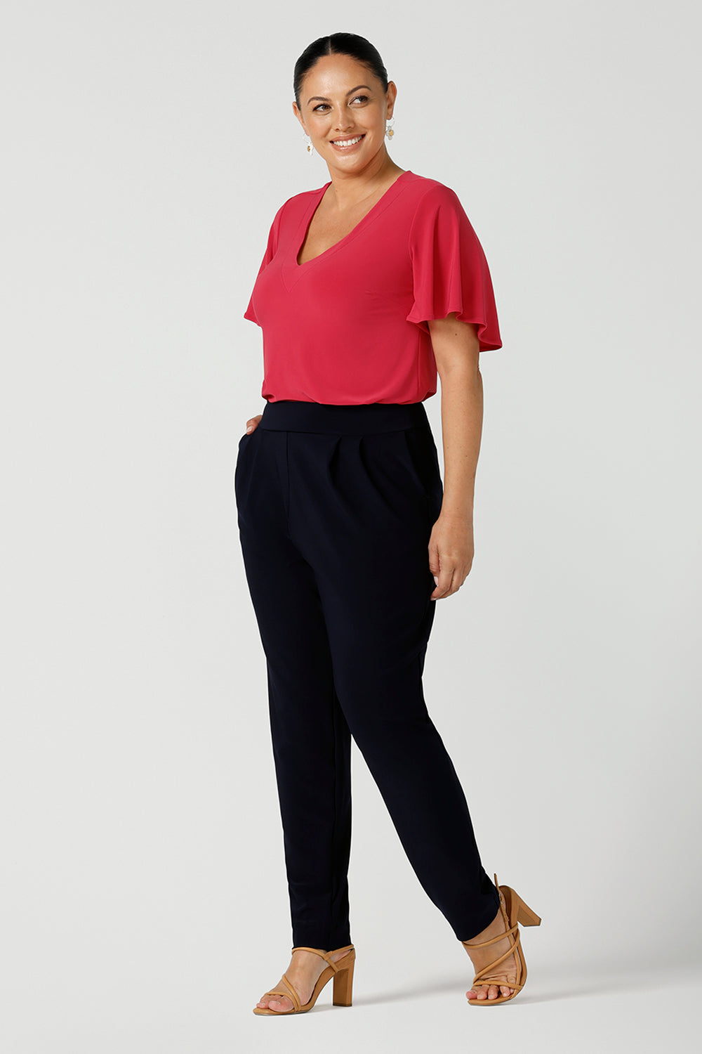 A happy size 12 woman wears jersey work pants in navy. Styled back with a fuchsia pink v-neck top. Comfortable corporate pants for women. Designed and made in Australia for Australian womenswear label Leina & Fleur. Inclusive size range 8 - 24. 