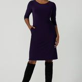 A size 10 woman wears the Audrey Dress in Amethyst. A purple Jersey dress made for women size 8-24. A comfortable workwear dress for petite to plus size 8-24. Curvy plus size workwear for women.