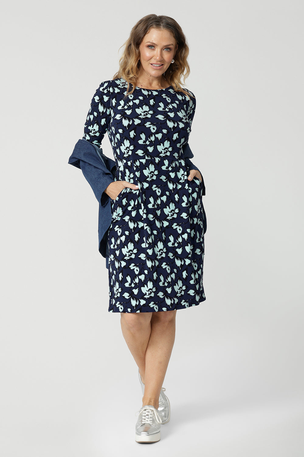  An over 40 woman wears a round neck shift dress in green and blue floral print. A good  casual dress for women, this jersey dress is worn with a vintage denim jacket. Both jacket and dress are made in Australia by Australian and New Zealand women's fashion brand, Leina & Fleur. Available in sizes 8 to 24, shop this casual dress with sleeves  in plus size and petite sizes.