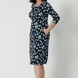 Showing a good dress for petite height women, a size 12 woman wears a round neck shift dress in green and blue floral print. A good workwear dress for women, this jersey dress is made in Australia by Australian and New Zealand women's fashion brand, Leina & Fleur. Available in sizes 8 to 24, shop this easy-care work dress in plus size and petite sizes.