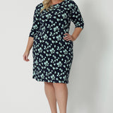 A size 18 woman wears a round neck plus size shift dress in green and blue floral print. A good workwear dress for women, this jersey dress is made in Australia by Australian and New Zealand women's fashion brand, Leina & Fleur. Available in sizes 8 to 24, shop this easy-care work dress in plus size and petite sizes.