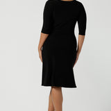 Close up of a size 10 woman wears the Audrey Dress, a black jersey round neckline dress with pockets and a boat neckline. Knee length style and easy care workwear for women. Made in Australia for women size 8 - 24.