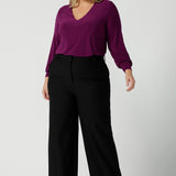 A size 18 woman wearing the Avery top in Magenta. A soft v-neck top with balloon sleeves and cuff detail. Made in Australia for women size 8 - 24. Styled back with a Kate pant in black