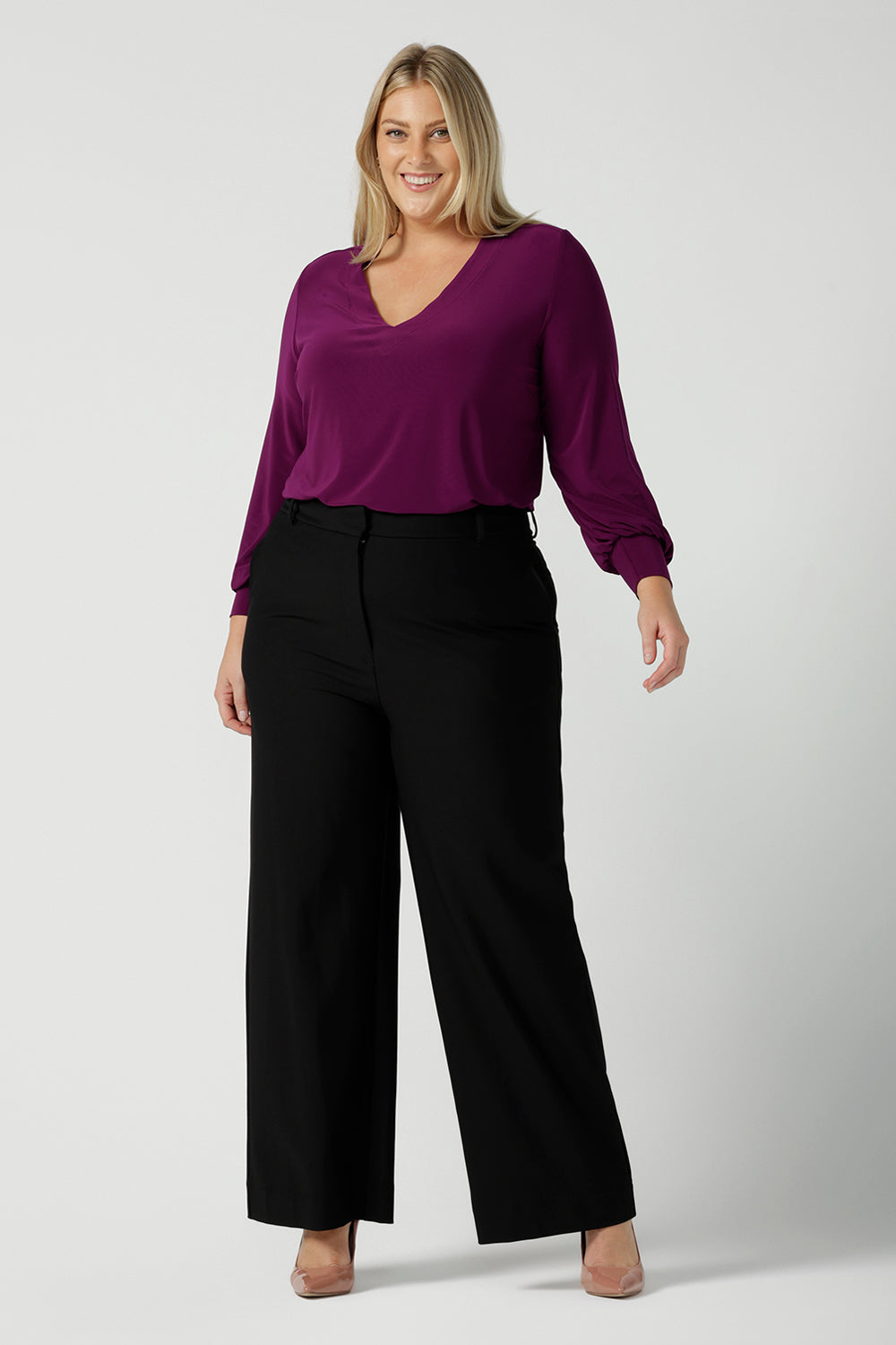 A size 18 woman wearing the Avery top in Magenta. A soft v-neck top with balloon sleeves and cuff detail. Made in Australia for women size 8 - 24. Styled back with a Kate pant in black