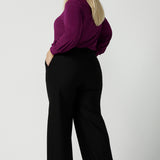 Back view of a size 18 woman wearing the Avery top in Magenta. A soft v-neck top with balloon sleeves and cuff detail. Made in Australia for women size 8 - 24. Styled back with a Kate pant in black