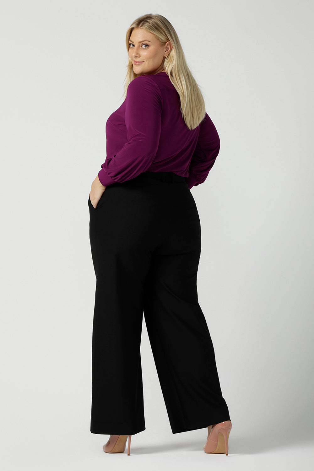 Back view of a size 18 woman wearing the Avery top in Magenta. A soft v-neck top with balloon sleeves and cuff detail. Made in Australia for women size 8 - 24. Styled back with a Kate pant in black