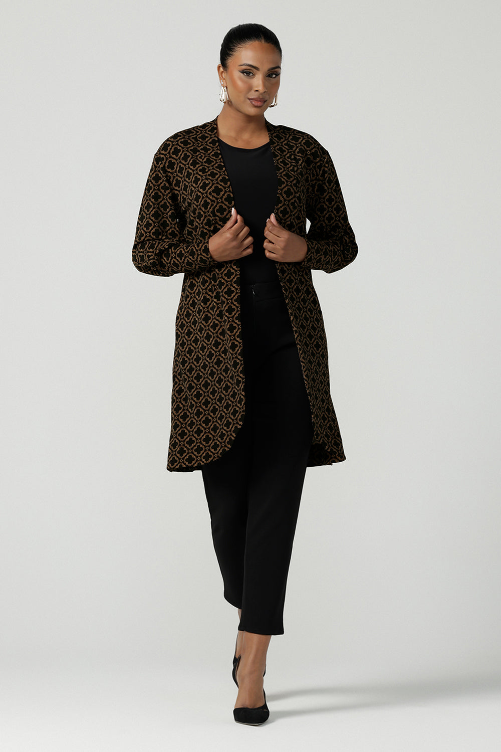 A size 10 woman wears the Bardon Duster in Zellige. A jersey longline cardigan with extended balloon sleeves and a curved hemline. Made in Australia for women size 8-24. In a beautiful tile print design with brown and black details.