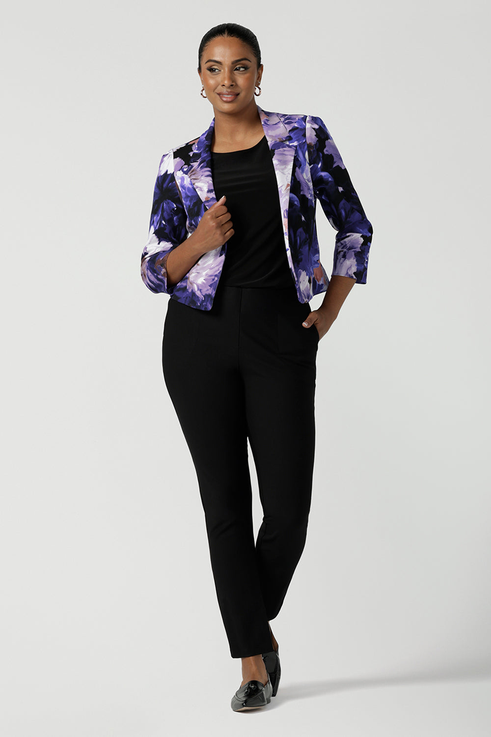 A size 10 woman wears a Benni Jacket in Jacaranda. With 3/4 sleeves and a floral purple print. Made in Australia for a size inclusive fashion label Leina & Fleur size 8-24.