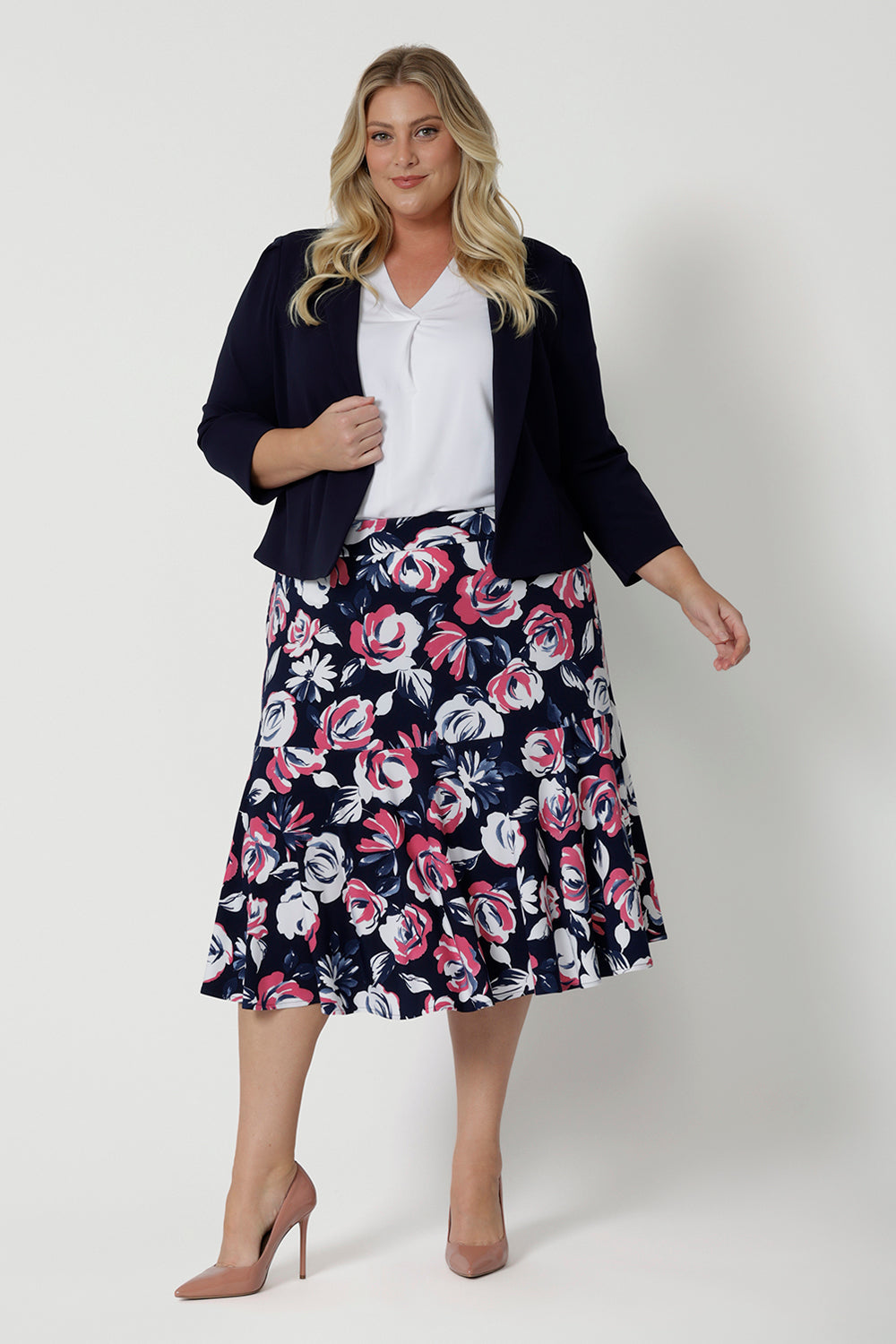 Full body front view of a plus sized model wearing a three quarter flowy skirt. The midi skirt has a floral design with white and pink flowers on a navy base. This easy to care fabric is dry touch jersey. Garments are Australian made for Australian and New Zealand women. Woman’s clothing retailer Leina & Fleur stock sizes from 8 to 24, which include plus and petite sizes.