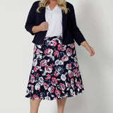 Full body front view of a plus sized model wearing a three quarter flowy skirt. The midi skirt has a floral design with white and pink flowers on a navy base. This easy to care fabric is dry touch jersey. Garments are Australian made for Australian and New Zealand women. Woman’s clothing retailer Leina & Fleur stock sizes from 8 to 24, which include plus and petite sizes.