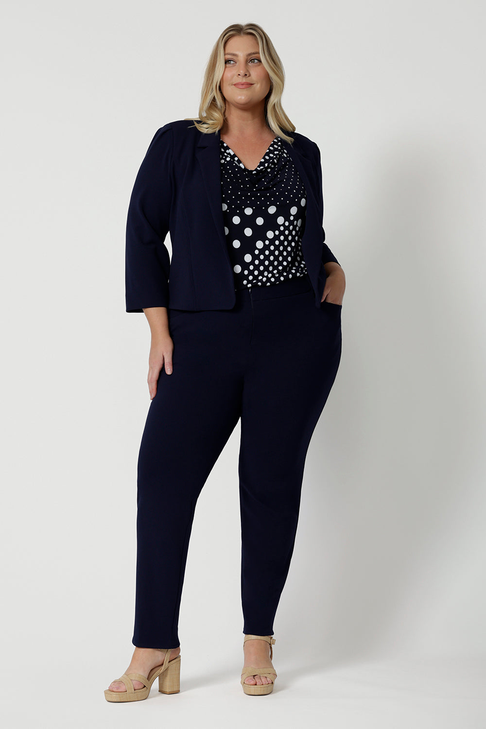 Showing a work top for curvy women, a size 18, plus size women wears a navy and white top with navy workwear suit . This sleeveless top has a cowl neck and is a comfortable top in stretch jersey fabric. Made in Australia by Australian and New Zealand clothing brand, Leina & Fleur, shop this top in petite to plus sizes. 