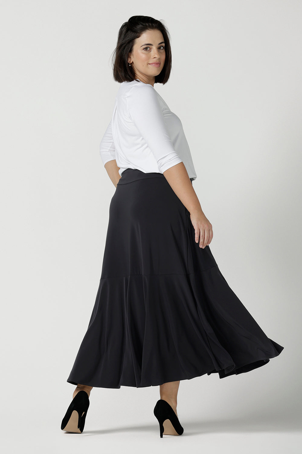 Back view of a size 10 wears the Berit Maxi skirt in Charcoal. A women's jersey work skirt with pockets in a charcoal colour. Made in Australia for women size 8 - 24. Styled back with the Jaime top in white bamboo with 3/4 sleeves.