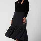 A size 12 woman wears the Thom top in Black a tie neck top with a V-neckline. Made in comfortable jersey have and made in Australia for women size 8 - 24. Styled back with a Berit Maxi Skirt in Charcoal