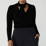 A size 12 woman wears the Thom top in Black a tie neck top with a V-neckline. Made in comfortable jersey have and made in Australia for women size 8 - 24.