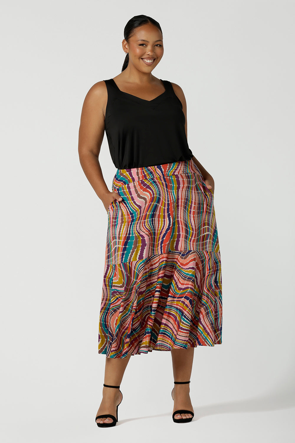 A curvy size 16 woman wears Berit Maxi skirt in Kaleidoscope styled back with a black Eddy Cami top. A rainbow coloured print with The Kaleidoscope print features a vibrant swirl of colour in all colours of the rainbow, pink, red, yellow, turquoise, brown and cobalt on a white base. Made in Australia for women size 8-24.