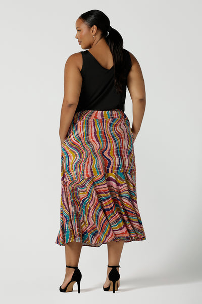 Back view of curvy size 16 woman wears Berit Maxi skirt in Kaleidoscope. A rainbow coloured print with The Kaleidoscope print features a vibrant swirl of colour in all colours of the rainbow, pink, red, yellow, turquoise, brown and cobalt on a white base. Made in Australia for women size 8-24.