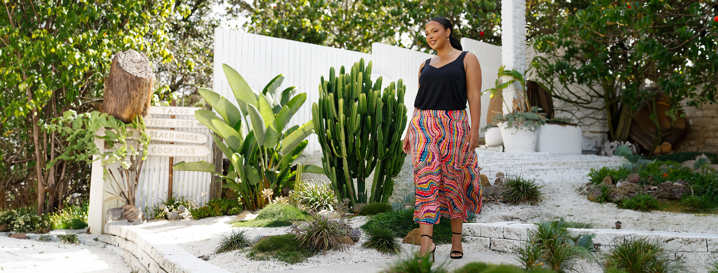A size 18, plus size woman wears a jersey maxi skirt in kaleidoscope print with black cami top as inspiration of summer outfits to wear for summer events and outings. 