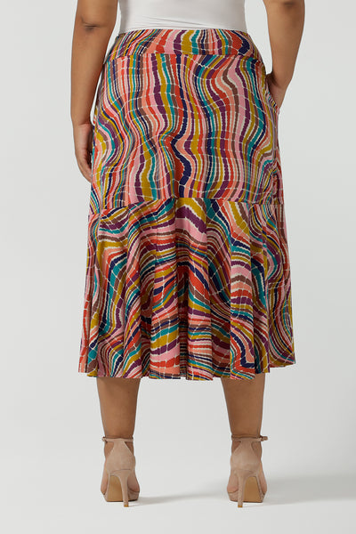 Back view of a size 12 woman wears Berit Maxi skirt in Kaleidoscope. A rainbow coloured print with The Kaleidoscope print features a vibrant swirl of colour in all colours of the rainbow, pink, red, yellow, turquoise, brown and cobalt on a white base. Made in Australia for women size 8-24.