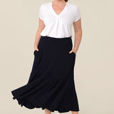 A woman wears a pull on, navy maxi skirt with ruffle hemline with a short sleeve bamboo jersey top in white. This black maxi skirt is a good workwear skirt or smart-casual skirt. Made in Australia in petite plus sizes for all curve of women's bodies..